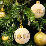 White ceramic bauble decorations with golden patterns and velvet ribbon hanging from branches of a Christmas tree.