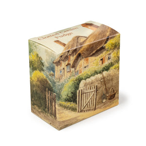 A square cardboard box of clotted cream fudge featuring an atmospheric pastel watercolour painting of Anne Hathaway's Cottage, with the garden gate open and a basket and gardening tools positioned next to the fence.