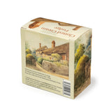 A square cardboard box of clotted cream fudge featuring an atmospheric pastel watercolour painting of Anne Hathaway's Cottage, showing the back side with the description of the painting.