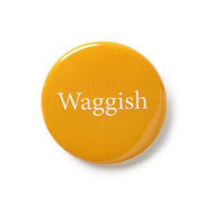 Yellow button badge with traditional pin fastening. White text says 'Waggish'.